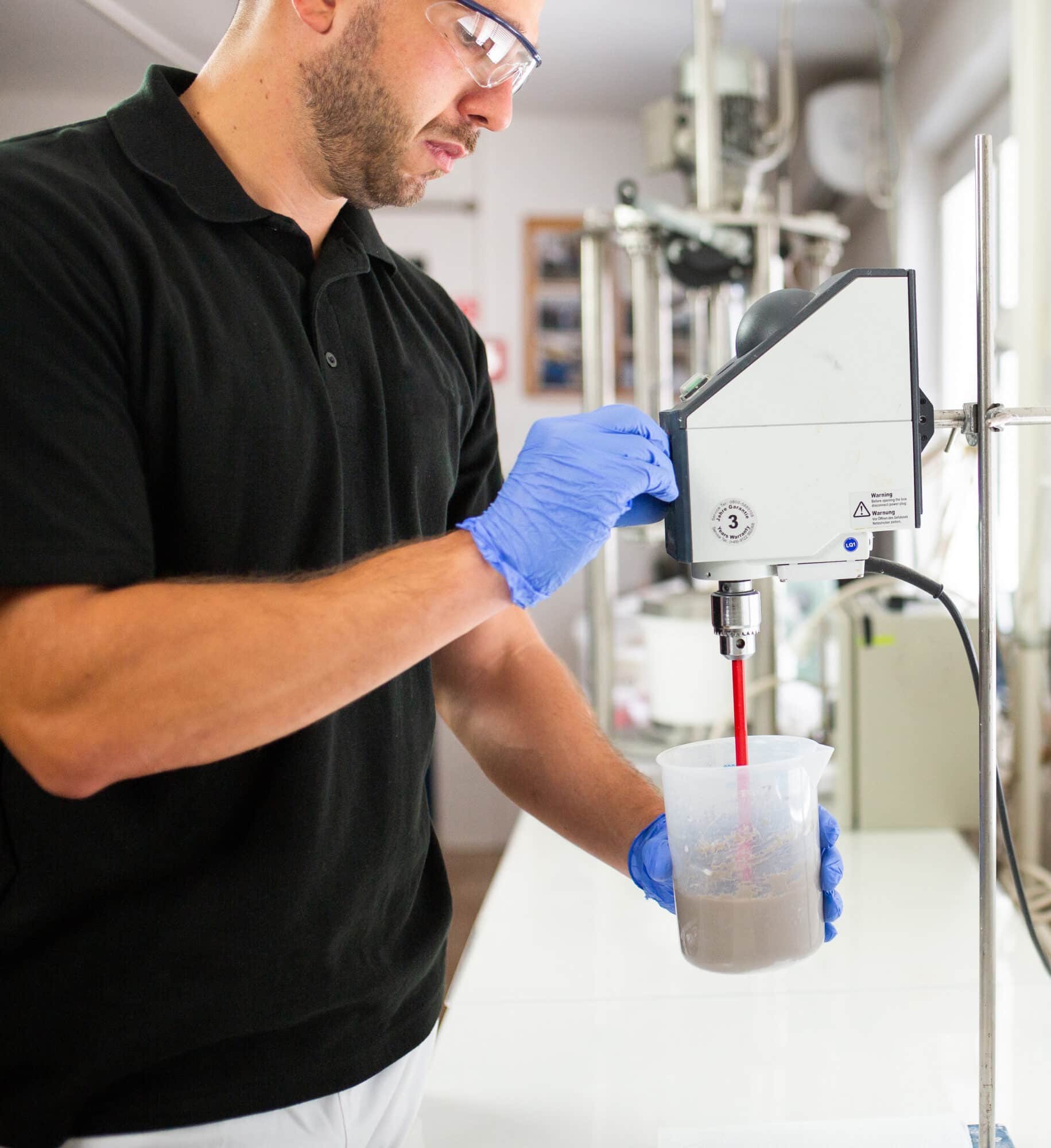 A person wearing safety glasses and gloves uses a laboratory mixer.